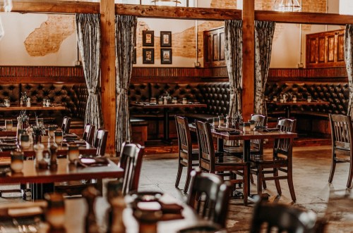 Cozy restaurant interior with wooden tables, chairs, and elegant decor, featuring booths and soft lighting.