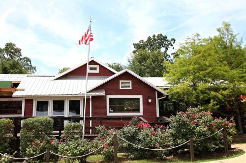 A red wooden building with a flag, surrounded by blooming rose bushes and trees, with an "Open" sign in the window.