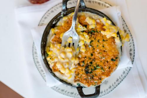 A cast-iron dish filled with creamy macaroni and cheese topped with corn and a crispy golden crust.