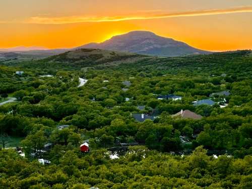Sunset over a lush green valley with a mountain in the background and scattered houses below.