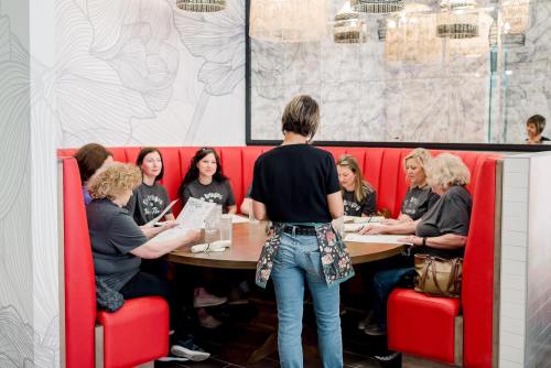 A group of women seated at a round table in a restaurant, reviewing menus with a server standing nearby.