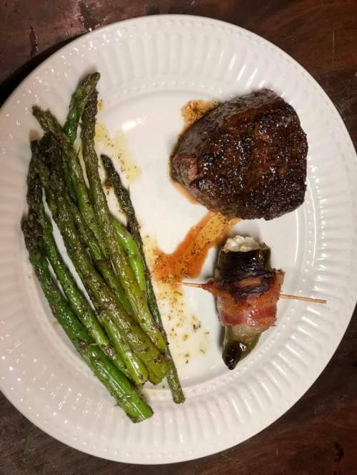 A plate featuring a grilled steak, asparagus, and a bacon-wrapped jalapeño popper.
