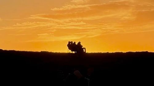 Silhouetted figures sitting on a hill against a vibrant sunset sky.