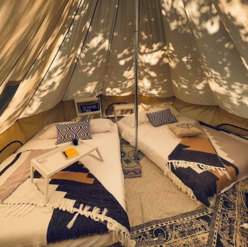 Cozy tent interior with two beds, decorative pillows, and a small table, surrounded by soft, dappled sunlight.