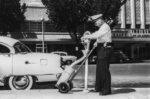 A police officer operates a parking meter beside a vintage car on a city street.
