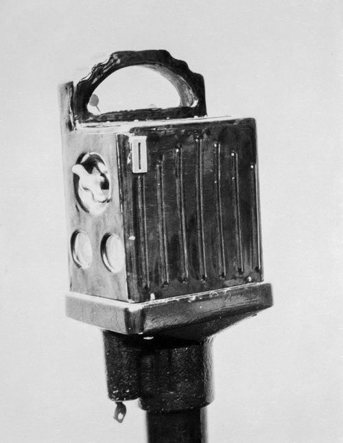 A vintage camera on a stand, featuring a boxy design with a handle and circular lenses.