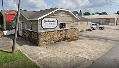 A small building with a stone facade and a sign reading "Stephen's Diner," surrounded by a parking lot and nearby structures.