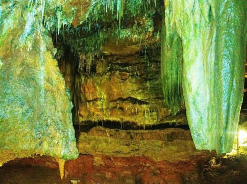 A colorful cave interior with stalactites and stalagmites, illuminated by soft lighting, showcasing natural rock formations.
