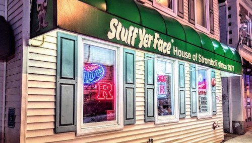 Exterior of "Stuff Yer Face" restaurant with green awning and neon signs, showcasing a cozy, inviting atmosphere.