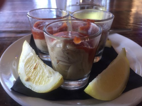 Three shot glasses filled with a creamy mixture, topped with sauce, served with lemon wedges on a plate.