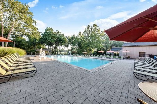 A serene outdoor pool area with lounge chairs, surrounded by trees and a clear blue sky.