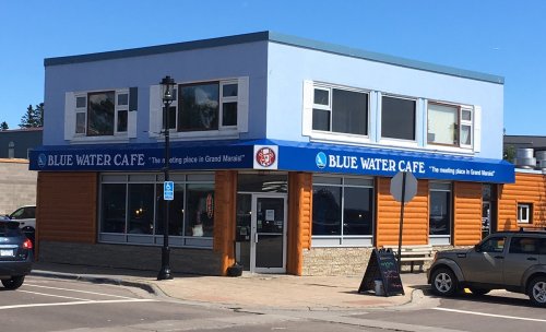 A blue and orange building with a sign reading "Blue Water Cafe" and outdoor seating in a sunny area.