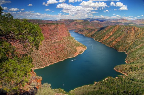 A scenic view of a winding river surrounded by red rock cliffs and lush greenery under a blue sky with fluffy clouds.