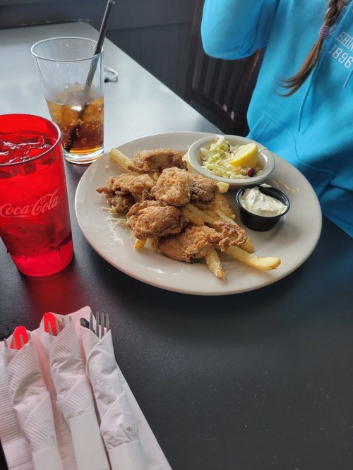 A plate of fried chicken with fries, coleslaw, and dipping sauce, alongside a red drink and utensils on a table.