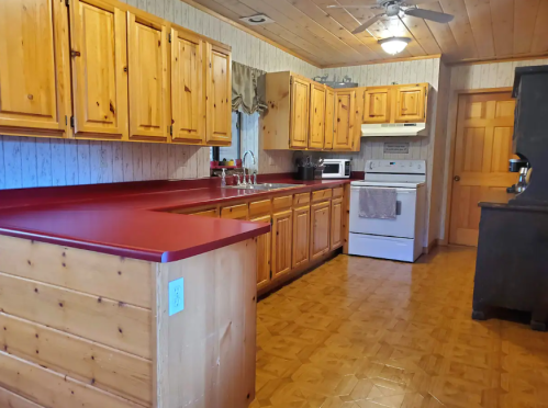 A cozy kitchen with wooden cabinets, red countertops, and white appliances, featuring a warm, rustic design.