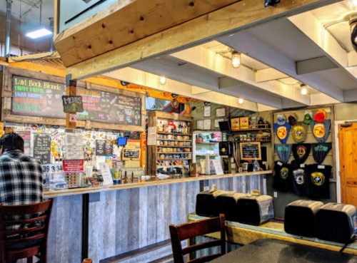 A cozy café interior with a wooden counter, colorful menus, and various drinks displayed on shelves.