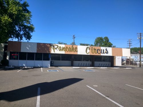 Exterior of a restaurant named "Pancake Circus," featuring a colorful sign and a parking lot under a clear blue sky.