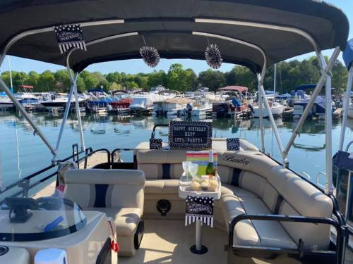 A decorated boat with seating and a table, surrounded by a marina filled with boats and trees in the background.