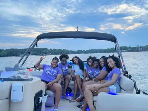 A group of seven women in matching shirts enjoying a boat ride on a lake, smiling and posing for the camera.