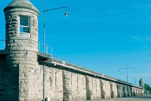 A stone wall with a watchtower under a clear blue sky, featuring a warning sign on the tower.