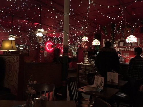 Cozy restaurant interior with red walls, string lights, and vintage lamps, creating a warm, inviting atmosphere.