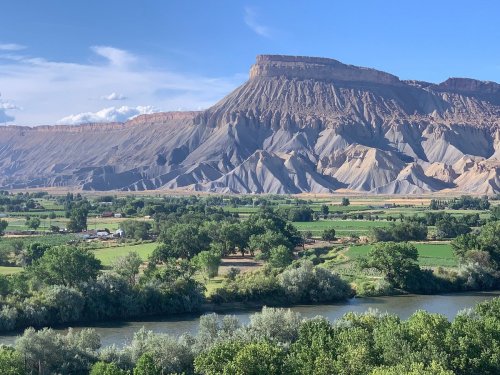 A scenic view of a large, flat-topped mountain with layered rock formations, surrounded by green fields and a river.