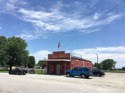 A red building with an American flag, surrounded by cars, under a blue sky with scattered clouds.