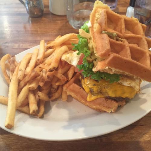 A plate featuring a waffle burger with lettuce, cheese, and an egg, accompanied by a side of crispy French fries.