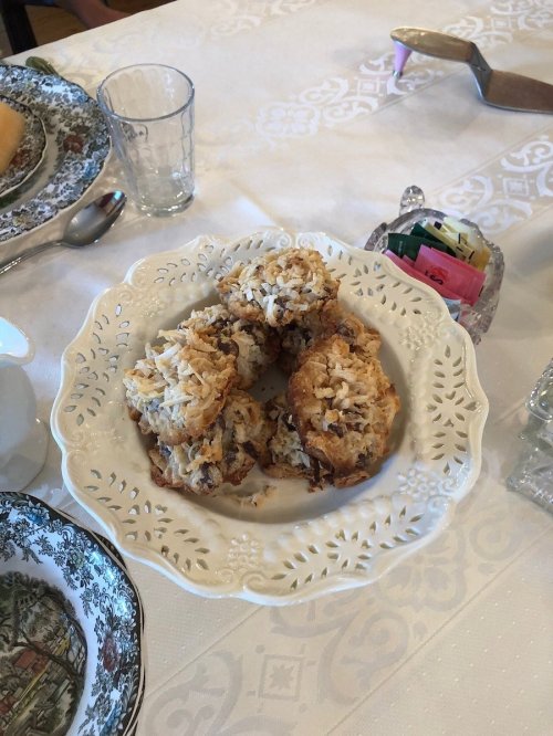 A decorative plate holds several coconut macaroons on a table set with fine china and glassware.