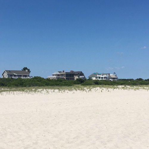 A sandy beach with several houses in the background under a clear blue sky.