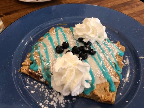 A blue plate with a dessert featuring a waffle topped with whipped cream, blueberries, and colorful icing.
