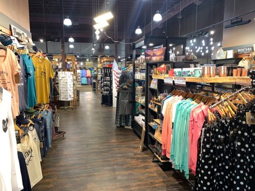 A retail store aisle filled with clothing and merchandise, featuring colorful shirts, accessories, and displays.