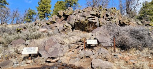 Rocky landscape with sparse vegetation and informational signs about the area, under a clear blue sky.