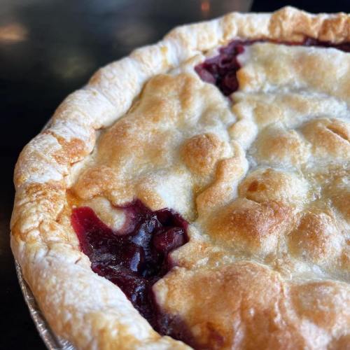 Close-up of a golden-brown cherry pie with a flaky crust and visible cherry filling peeking through.