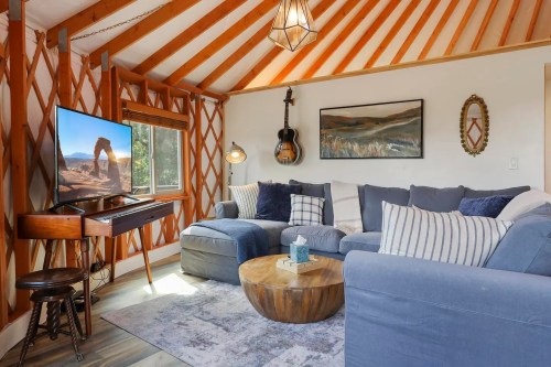 Cozy living room with a blue sectional sofa, wooden coffee table, TV, and guitar, featuring warm wood accents and decor.