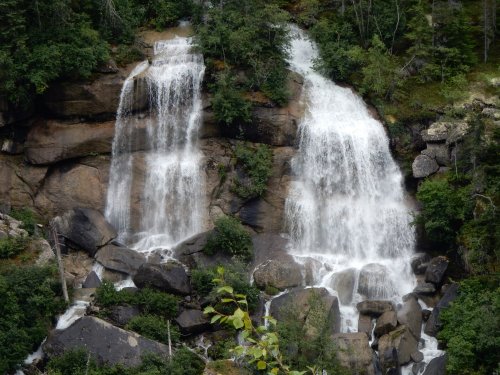 A scenic view of two waterfalls cascading over rocky cliffs, surrounded by lush green foliage.