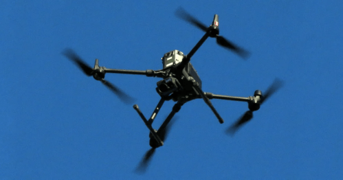 A drone with multiple rotors flying against a clear blue sky.
