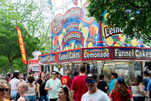 A busy food stand selling funnel cakes and lemonade, with a crowd of people enjoying the fair atmosphere.