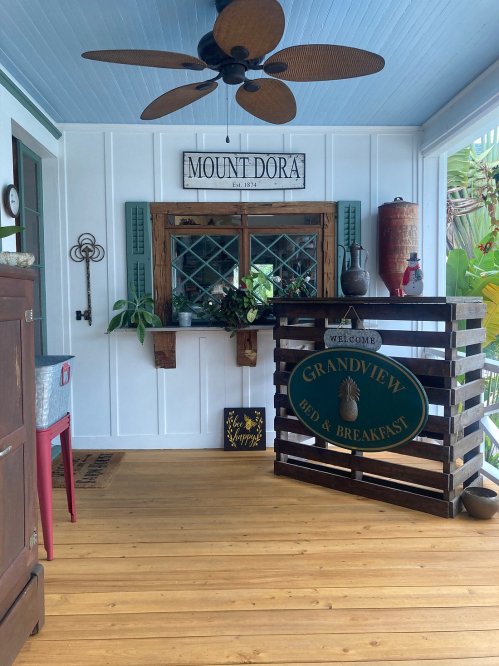 A cozy porch with a wooden floor, fan, and a sign for Grandview Bed & Breakfast, featuring plants and decorative elements.