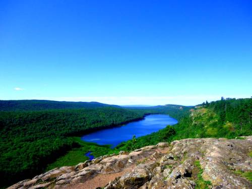 A scenic view of a blue lake surrounded by lush green forests under a clear blue sky.