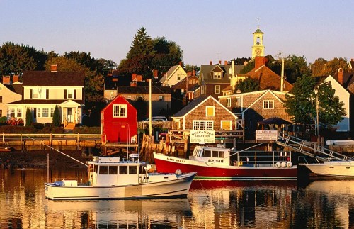 A serene harbor scene with fishing boats and colorful houses reflecting in calm water during sunset.
