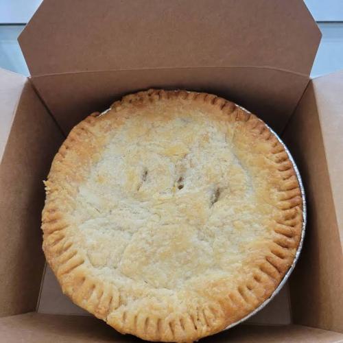 A freshly baked pie in a cardboard box, featuring a golden, flaky crust.