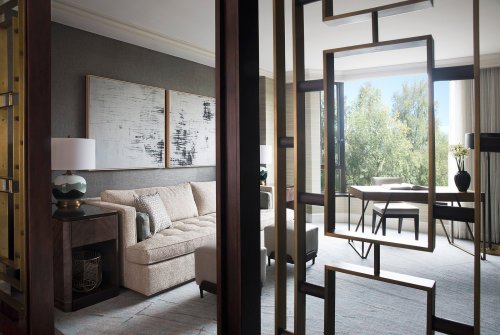 Modern hotel suite featuring a cozy sofa, artwork, and a workspace with large windows overlooking greenery.