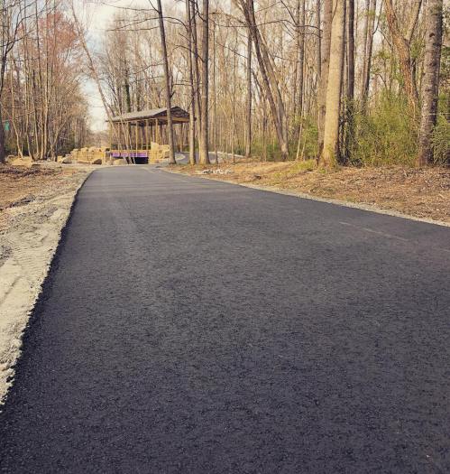 A newly paved path leads through a wooded area, with a gazebo visible in the distance.