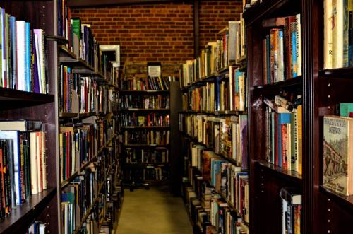 A narrow aisle between tall bookshelves filled with various books in a cozy library setting.