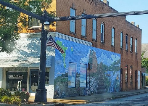 A colorful mural depicting landscapes and a train track on the side of a brick building, with an American flag nearby.