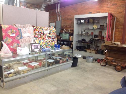 A display of quilts and vintage items in a rustic room with brick walls and various antiques on shelves.