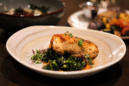 A beautifully plated dish featuring a piece of chicken on a bed of greens, garnished with herbs.