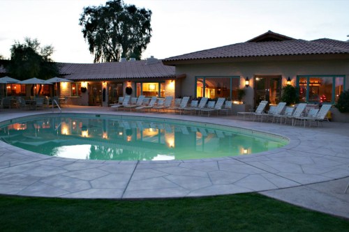 A serene pool area with lounge chairs, surrounded by a cozy building and trees at dusk.