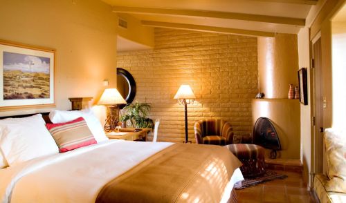 Cozy bedroom with a large bed, armchair, and a small fireplace, featuring warm colors and soft lighting.